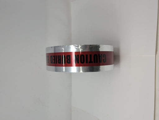 Close-up of a metallic utility tape roll featuring a red center stripe with the black printed text CAUTION BURIED E and silver reflective edges.