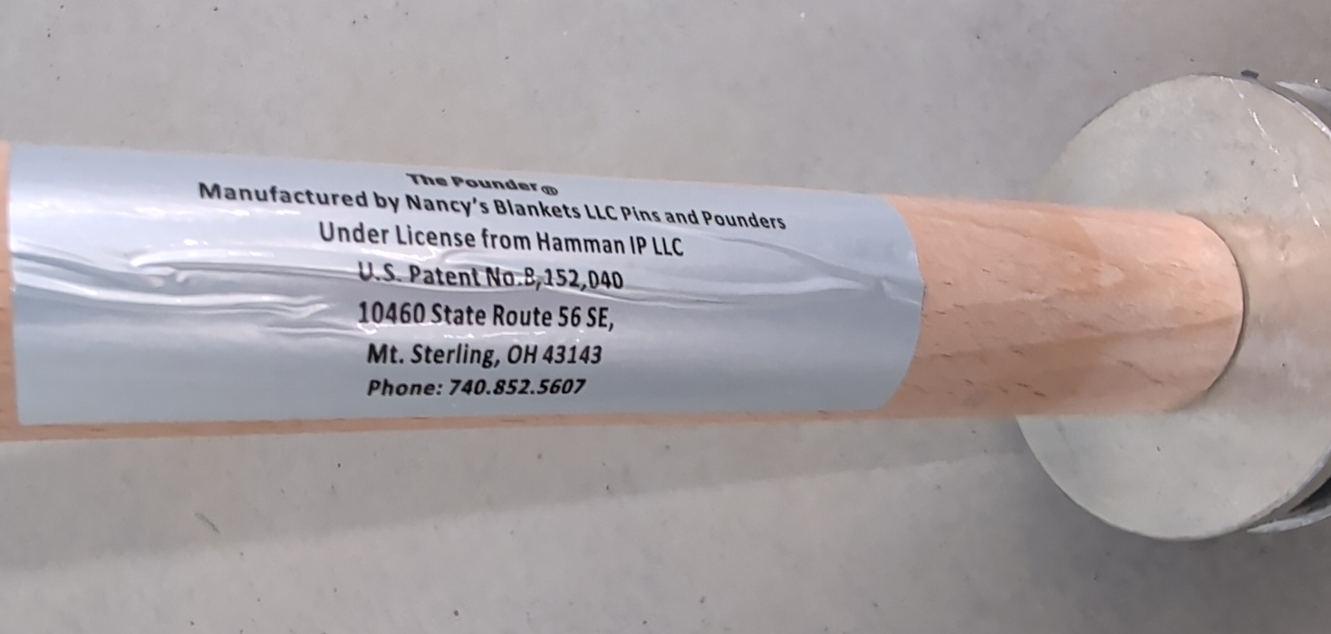 A close-up view of a cylindrical wooden handle featuring a silver adhesive label with manufacturer and patent information and a metallic circular disc attachment.