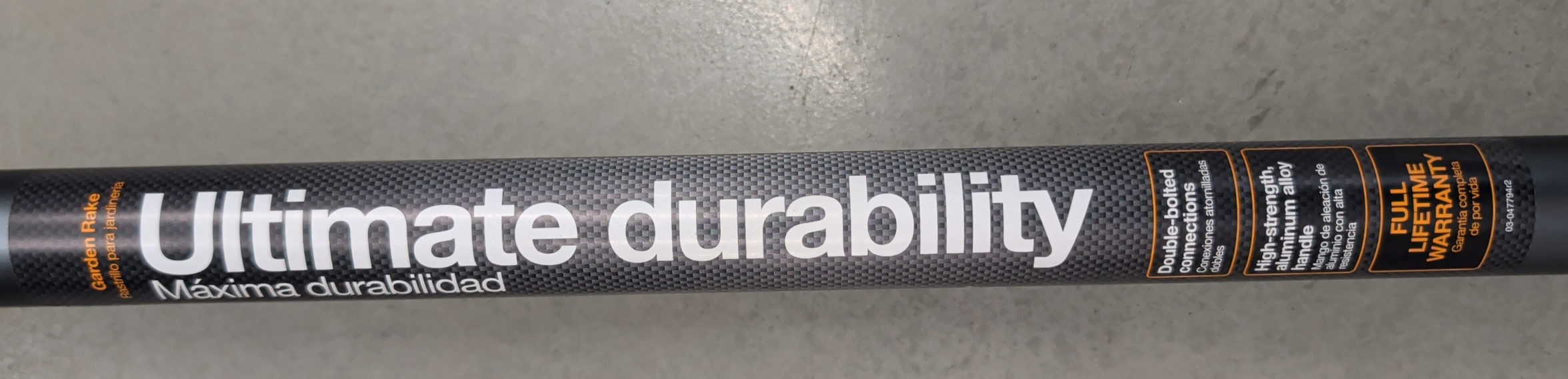 Close-up of the Fiskars PRO garden rake handle and connection point showing the carbon-fiber-look finish, double-bolted construction, and warranty information.